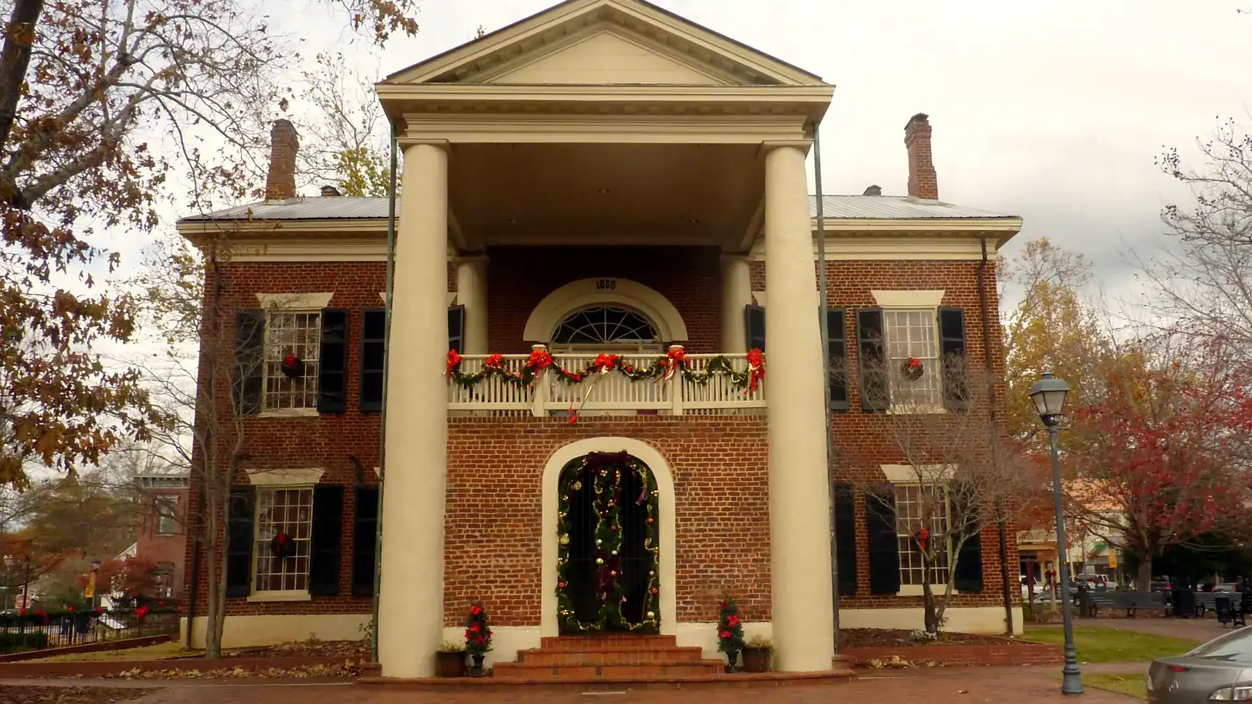 Front portico of the Dahlonega Gold Museum with garland on the balcony rail, a garland-framed arched doorway and wreaths in the windows.