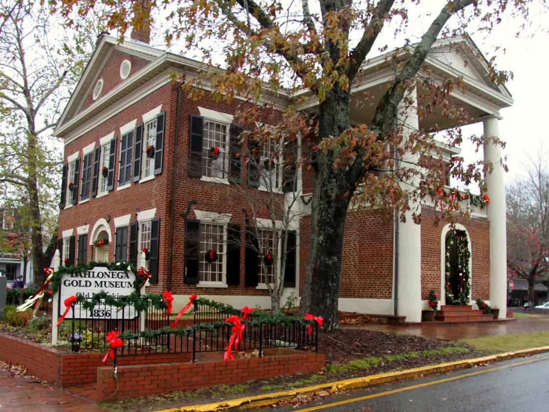 Red-brick Dahlonega Gold Museum with Christmas wreaths in the windows, garland on the fence and doorway, and its 1836 sign out front.