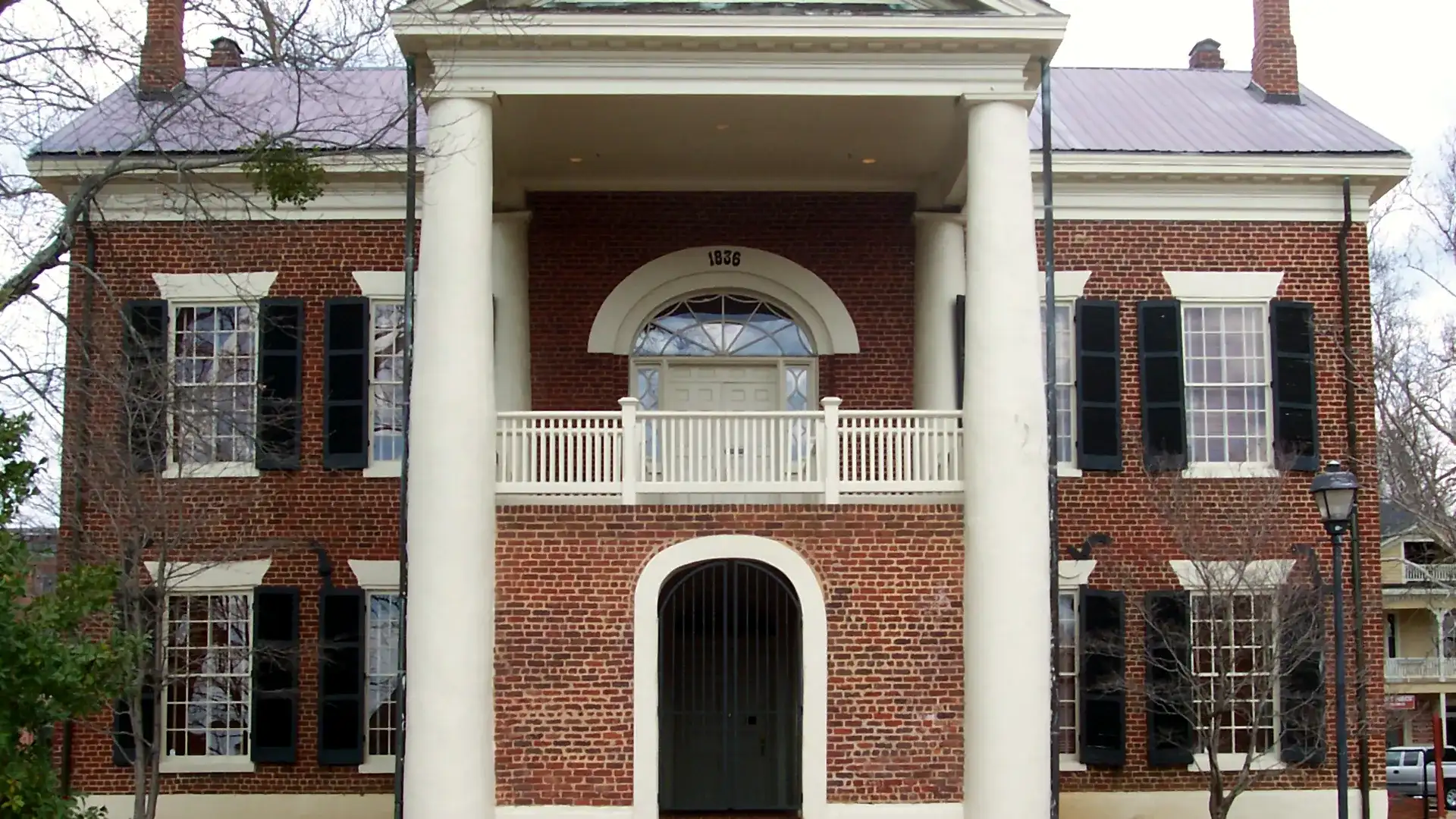 Straight-on view of the Dahlonega Gold Museum's white-columned portico, with an 1836 fanlight and an arched gated doorway, in winter.