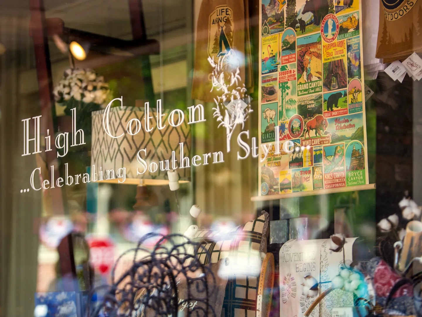 Shop window lettered 'High Cotton ...Celebrating Southern Style' with a national parks poster and cotton bolls on display inside.