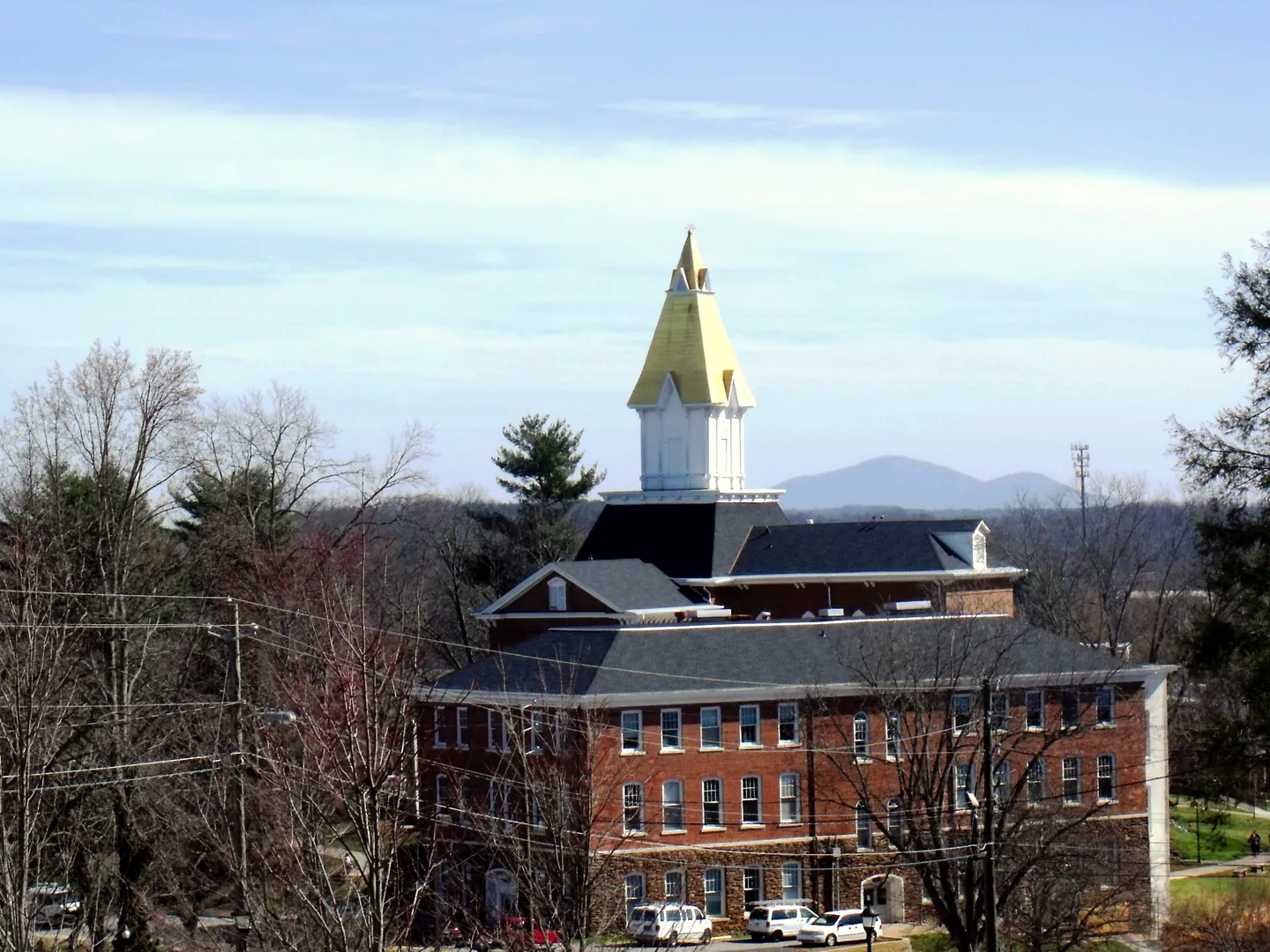 Gold-topped white steeple of Price Memorial Hall at the University of North Georgia, with a blue mountain on the horizon behind it.