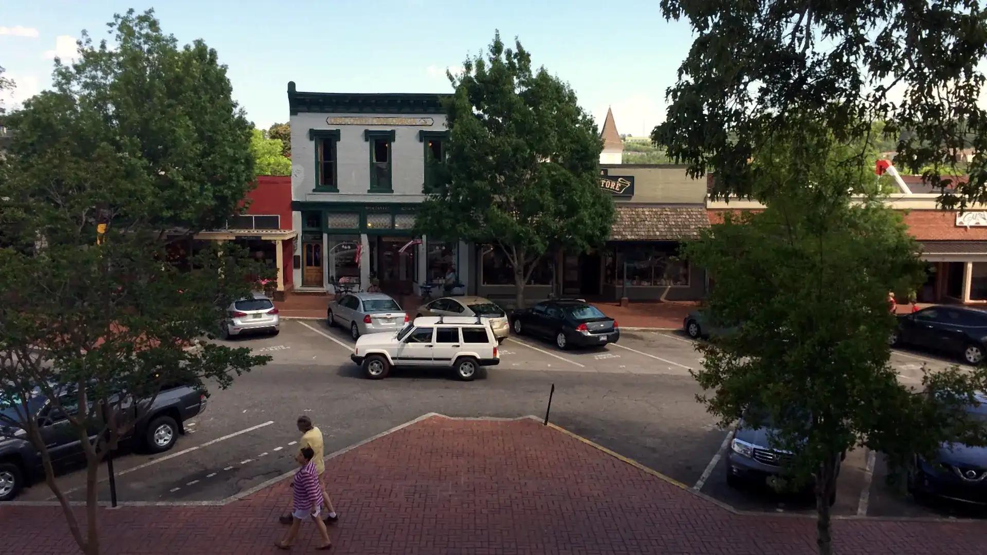 Elevated summer view of shops on Dahlonega's public square, with a white storefront signed 'Discover Dahlonega', parked cars and a brick plaza.