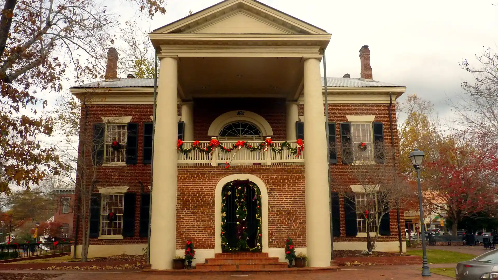Front portico of the Dahlonega Gold Museum with garland on the balcony rail, a garland-framed arched doorway and wreaths in the windows.