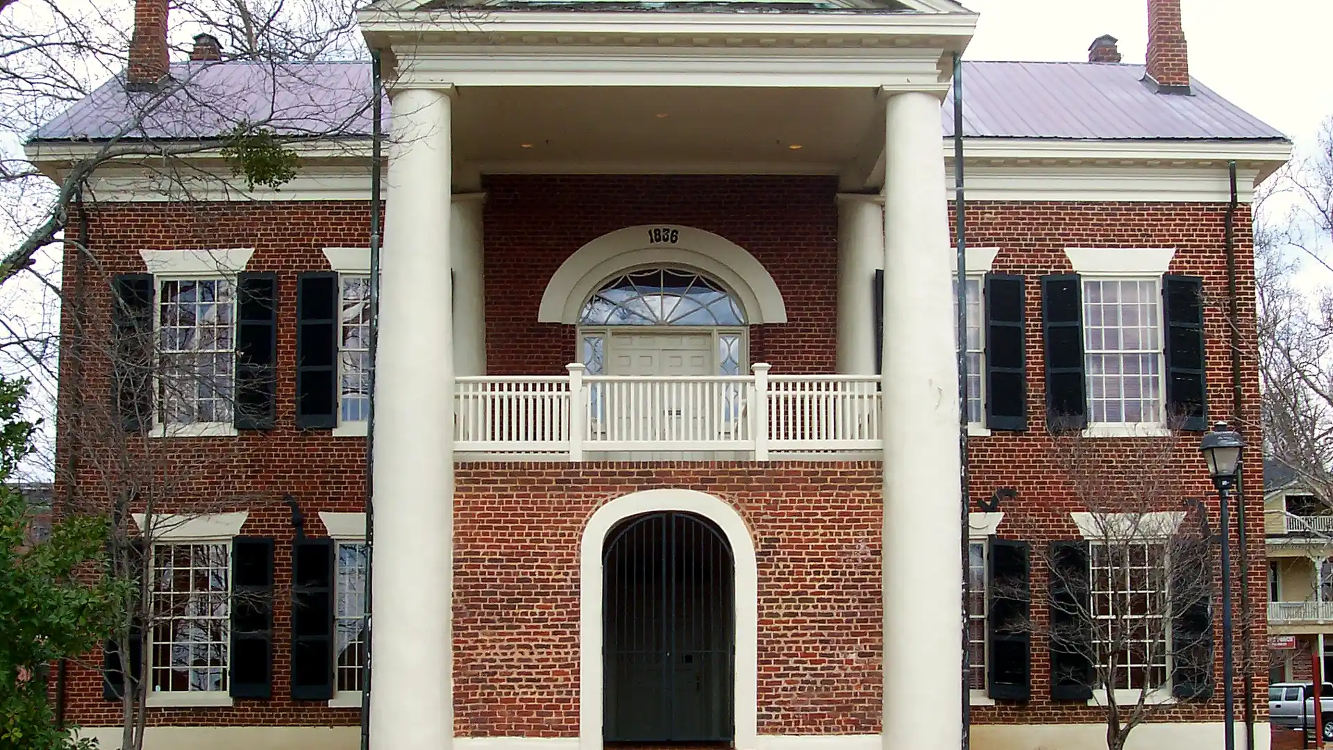 Straight-on view of the Dahlonega Gold Museum's white-columned portico, with an 1836 fanlight and an arched gated doorway, in winter.