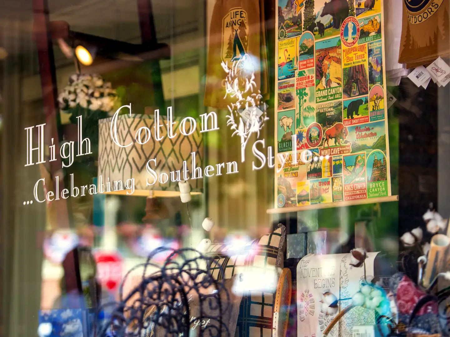 Shop window lettered 'High Cotton ...Celebrating Southern Style' with a national parks poster and cotton bolls on display inside.